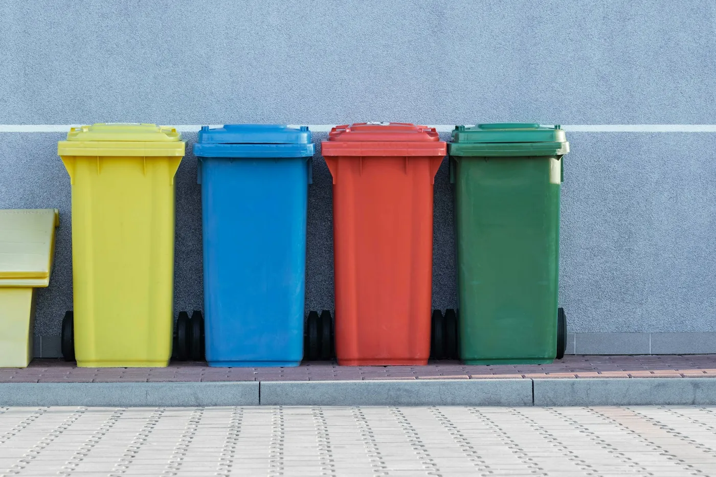 Quattro bidoni colorati per la raccolta differenziata allineati contro un muro grigio